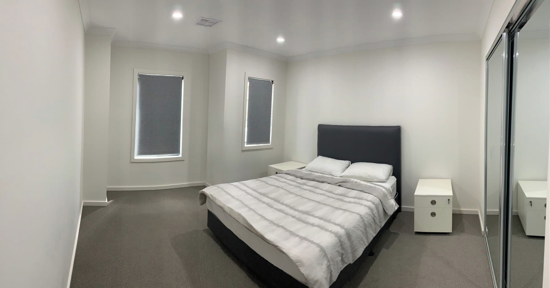 Ein modernes Schlafzimmer mit einem großen Bett, zwei Nachttischen und zwei Fenstern.