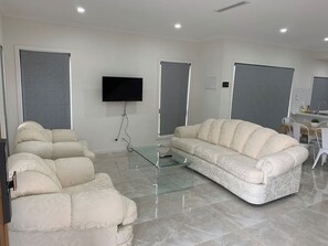 A modern living room with a sofa, armchairs, a glass coffee table, and a flat-screen TV mounted on the wall.