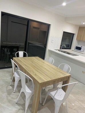 A modern kitchen with a wooden dining table and white chairs, a microwave, and a sink.