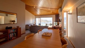 Amplia sala de estar con techo de madera, una gran mesa de comedor y vistas a un lago.