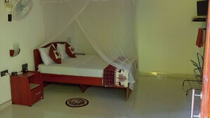 A bedroom with a bed under a mosquito net, a bedside table, a fan, and a small rug. - solitary resort  (Ella)