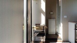Un pasillo estrecho con un banco de madera, una mesita y una pequeña zona de kitchenette con un fregadero y alacenas.