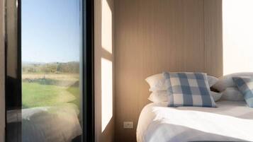 Ein Schlafzimmer mit großem Fenster, einem Bett mit weißer Bettwäsche und einem karierten Kopfkissen.