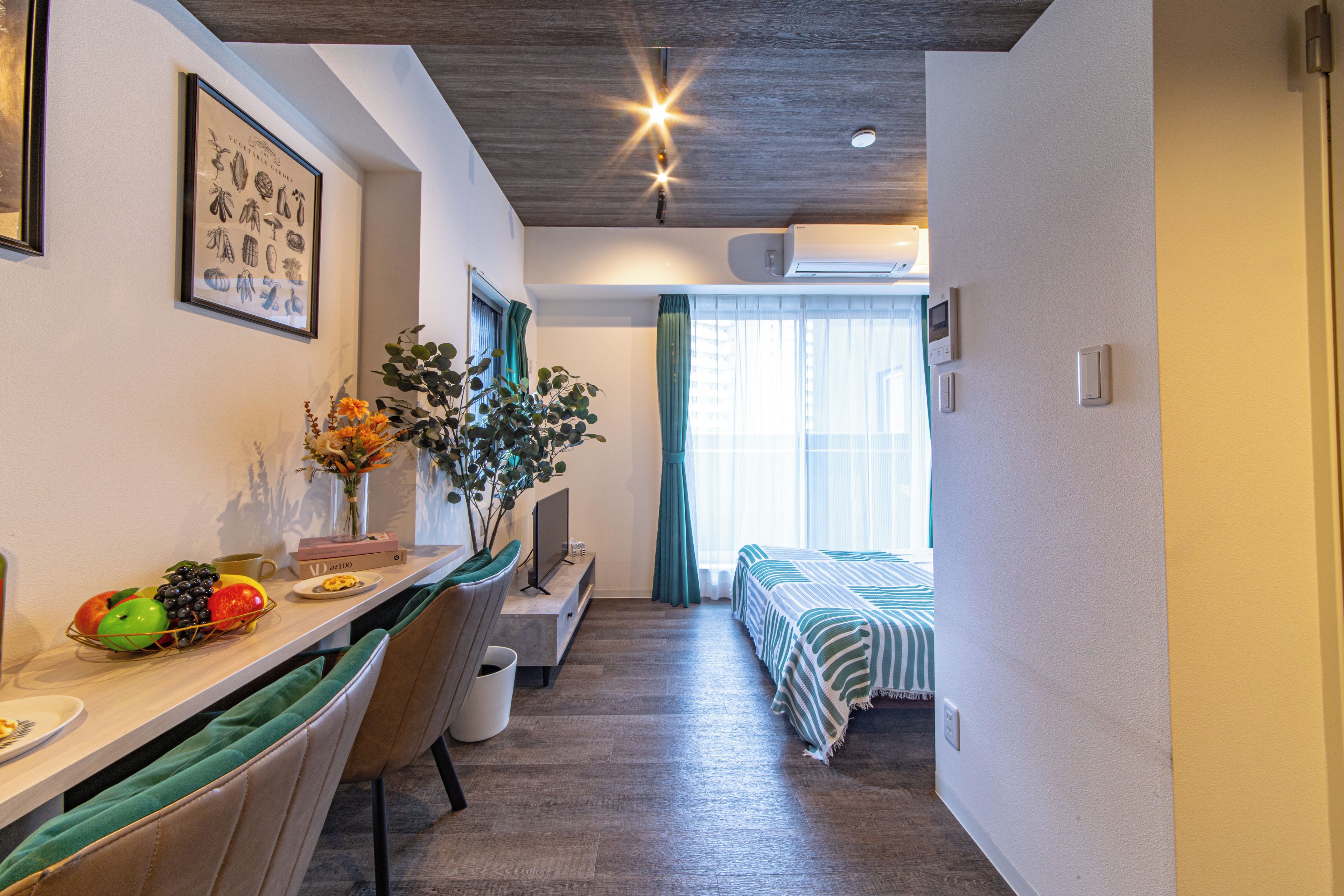 Una stanza compatta con un'area pranzo, un letto con copriletto a righe e una finestra con tende.