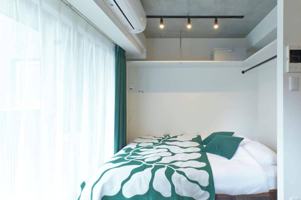 Quarto de hotel com cama, janela com cortinas, aparelho de ar condicionado e luminária no teto.