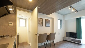 A modern living room with a kitchen area, wooden flooring, a dining set, and a flat-screen TV. - MATSUMIZAKA HILL by Tranova (Tokyo)