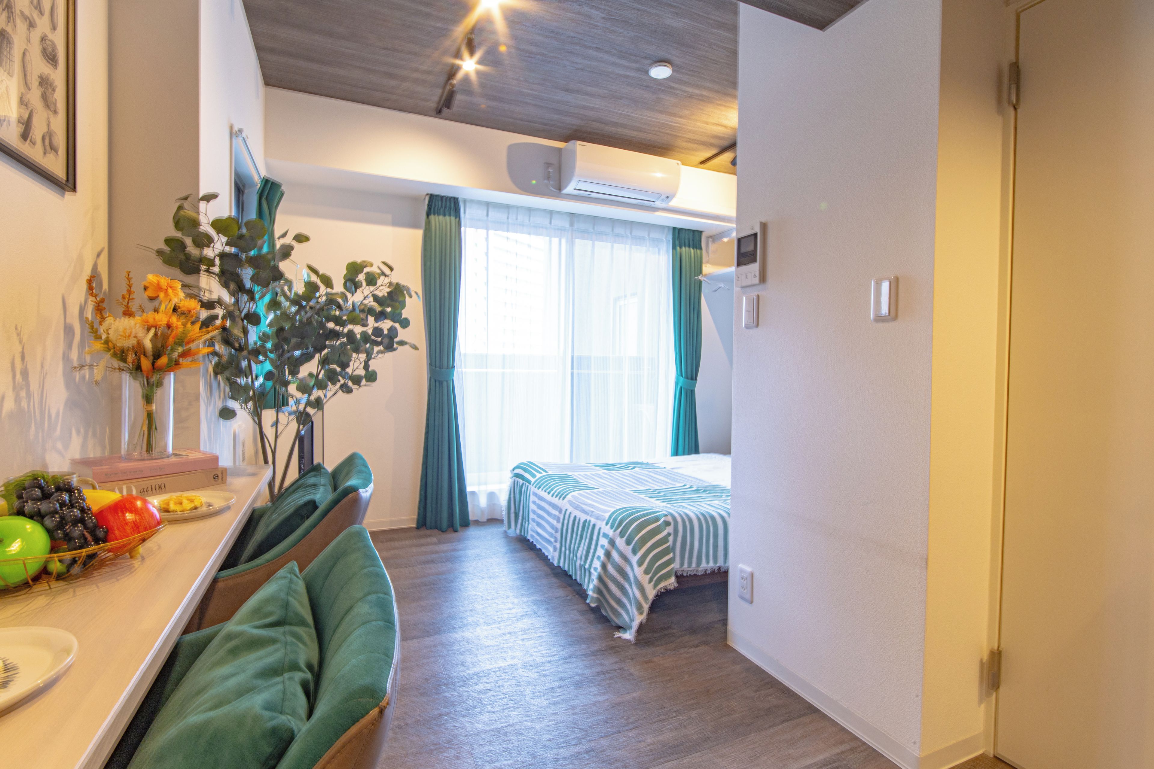 A hotel room with a bed, a desk with a chair, a vase with flowers, and a window with curtains.