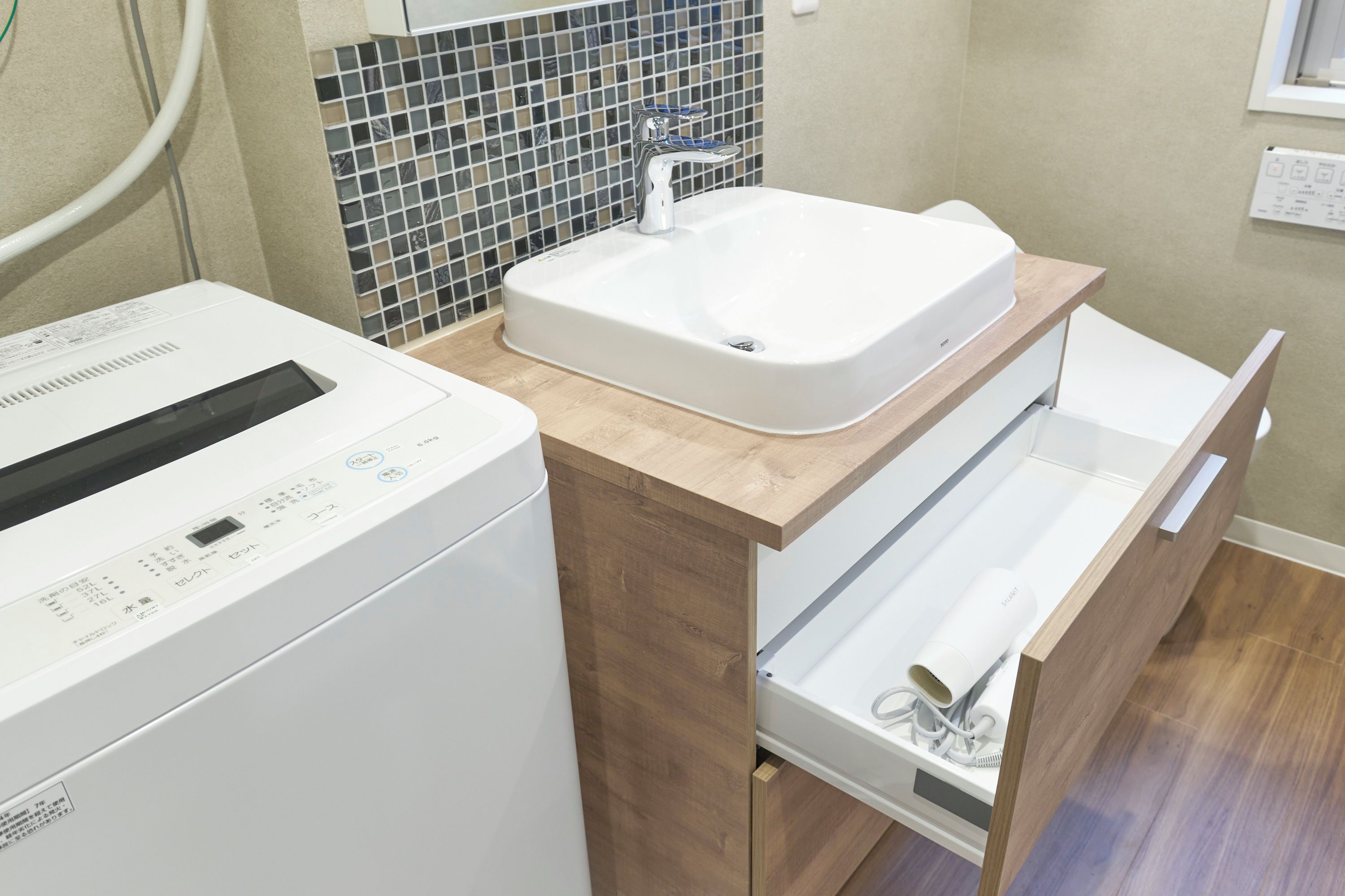 Un baño moderno con lavadora integrada, un lavamanos y un mueble de tocador de madera con un cajón.