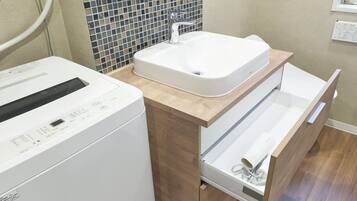 Un baño moderno con lavadora integrada, un lavamanos y un mueble de tocador de madera con un cajón.