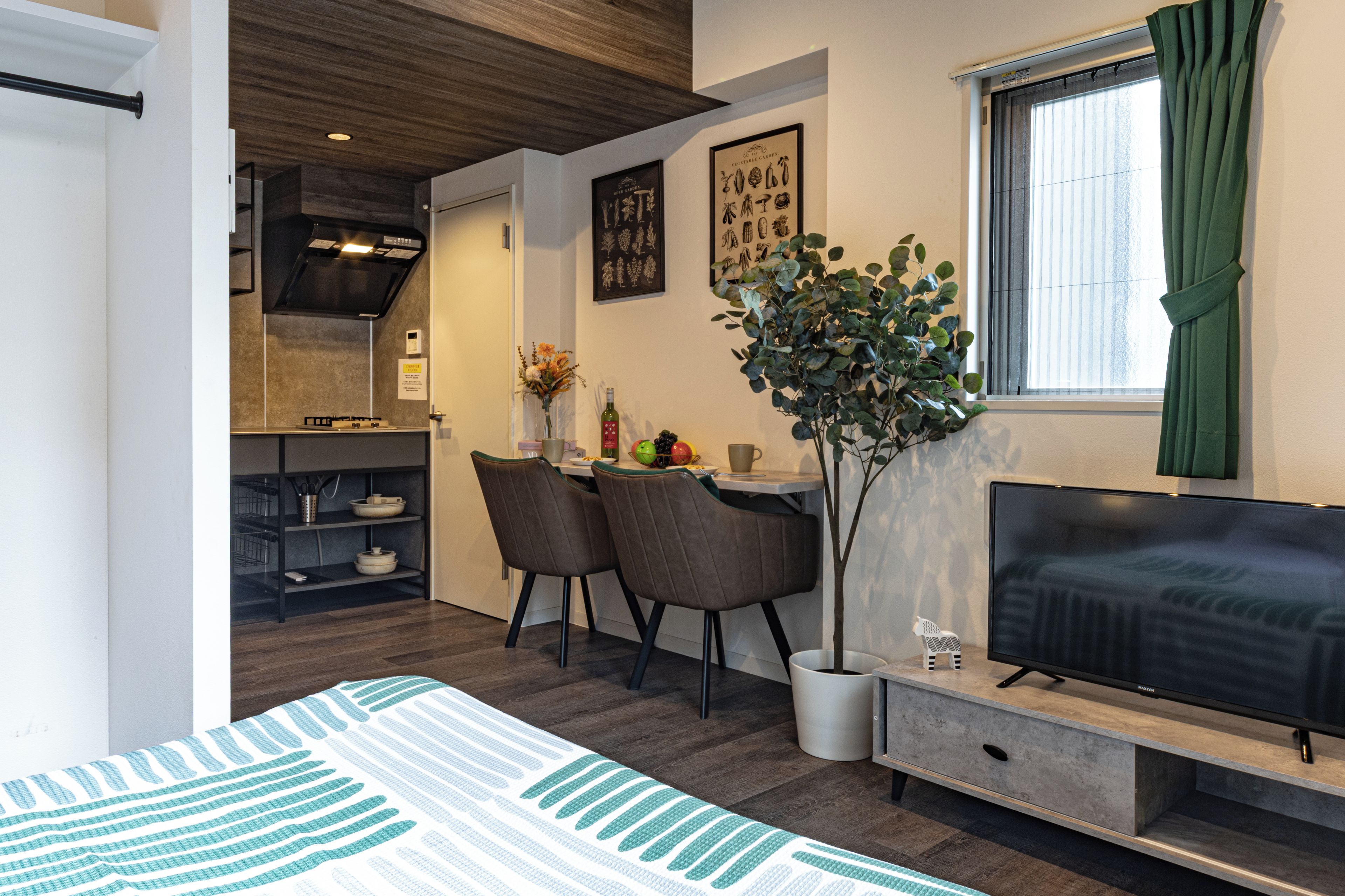A modern living room with a flat-screen TV, a dining area with chairs and a table, and a kitchen with a stove and cabinets.