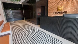 A reception area with a geometric patterned floor, a reception desk, and a brick wall with the name 'FIAMENE' displayed.