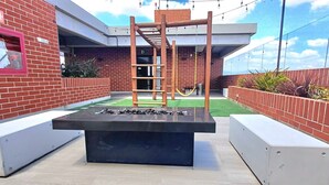 A courtyard with a fire pit, a wooden climbing structure, and a brick wall.
