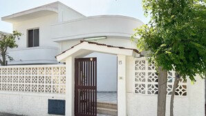 A modern two-story house with a white exterior, a dark brown gate, and a tree in front. - Villetta Zagara | outdoor space, a/c, 2 bedrooms (Porto Cesareo)