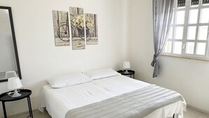 A bedroom with a bed, a nightstand, a lamp, and a window with curtains. - Villetta Zagara | outdoor space, a/c, 2 bedrooms (Porto Cesareo)