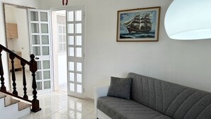 A room with a grey sofa, a painting of a ship, and a white door with glass panels. - Villetta Zagara | outdoor space, a/c, 2 bedrooms (Porto Cesareo)