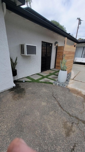 Une maison moderne avec une porte noire, un petit jardin agrémenté d’un pot de fleurs et une allée en béton.