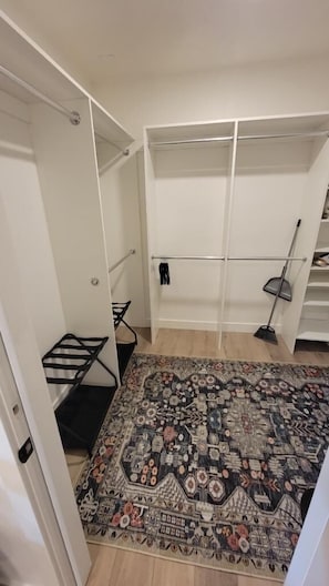 Un dressing accessible sans porte, doté d’étagères ouvertes, d’une tringle à vêtements et d’un tapis à motifs sur le sol.