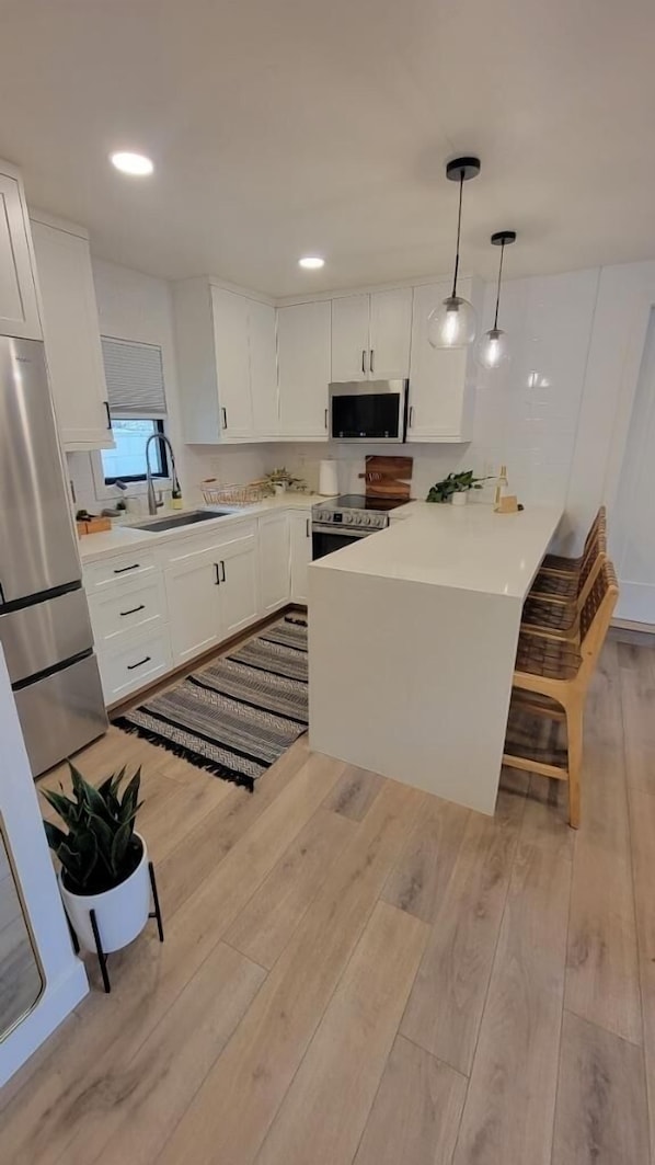 Une cuisine moderne avec des meubles blancs, un îlot central, des appareils en acier inoxydable et un banc en bois.