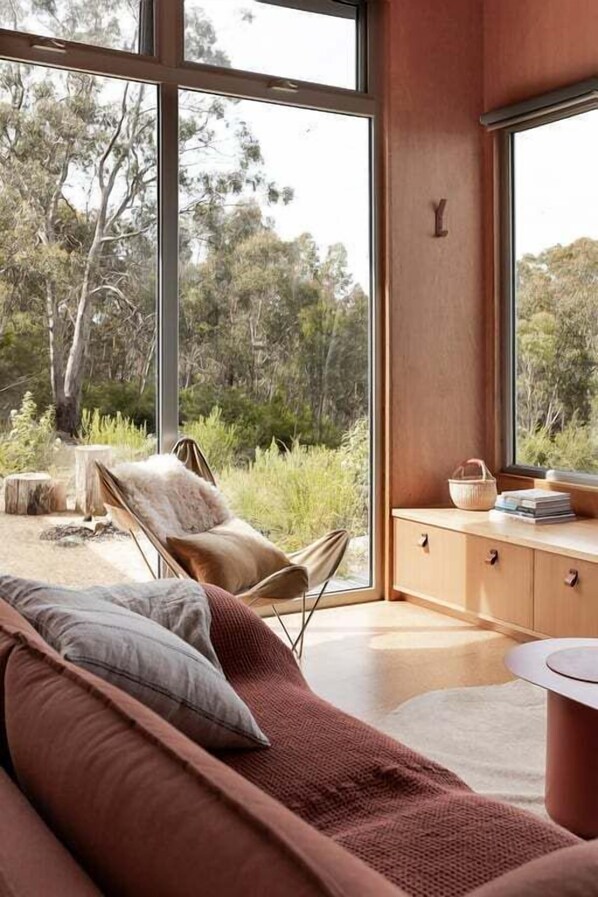 Ein modernes Zimmer mit großen Fenstern, einem Holzkabinett und einer gepolsterten Sitzecke.