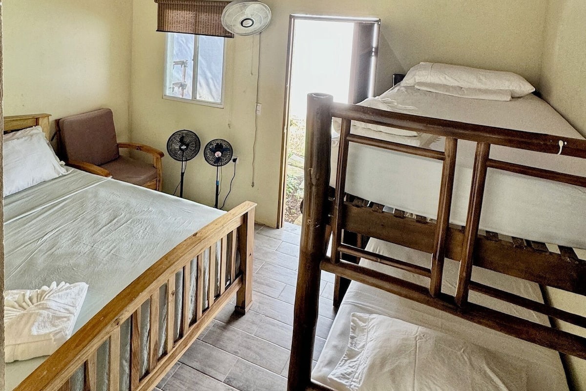 A room with a bunk bed, a single bed, a chair, and a fan.