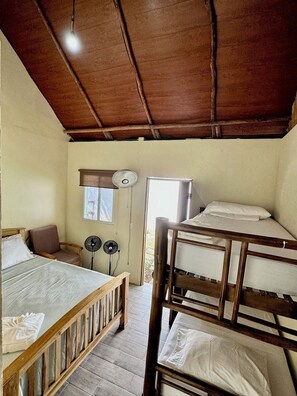 A room with a bunk bed, a single bed, a chair, and a fan. - The Grand Mango (Tola)