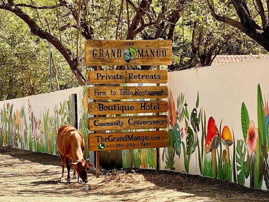 Un letrero de madera que anuncia diversos servicios, incluyendo retiros privados, restaurante con productos de la granja, hotel boutique y una reserva comunitaria.