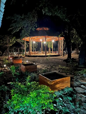 A gazebo with a tiled roof and wooden pillars, surrounded by stone pathways and wooden planters. - The Grand Mango (Tola)