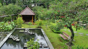 A tranquil garden with a pond, a wooden bench, and a gazebo. - Hotel Cianjur Cipanas (Cipanas)