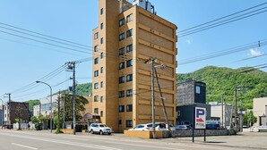 A multi-story building with a parking sign, a street, and a hillside in the background. - Fine court Yamahana (Sapporo)