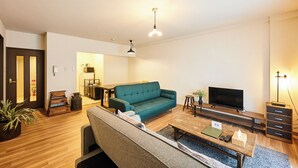 A modern living room with a teal sofa, a wooden coffee table, a TV, and a small side table. - Fine court Yamahana (Sapporo)