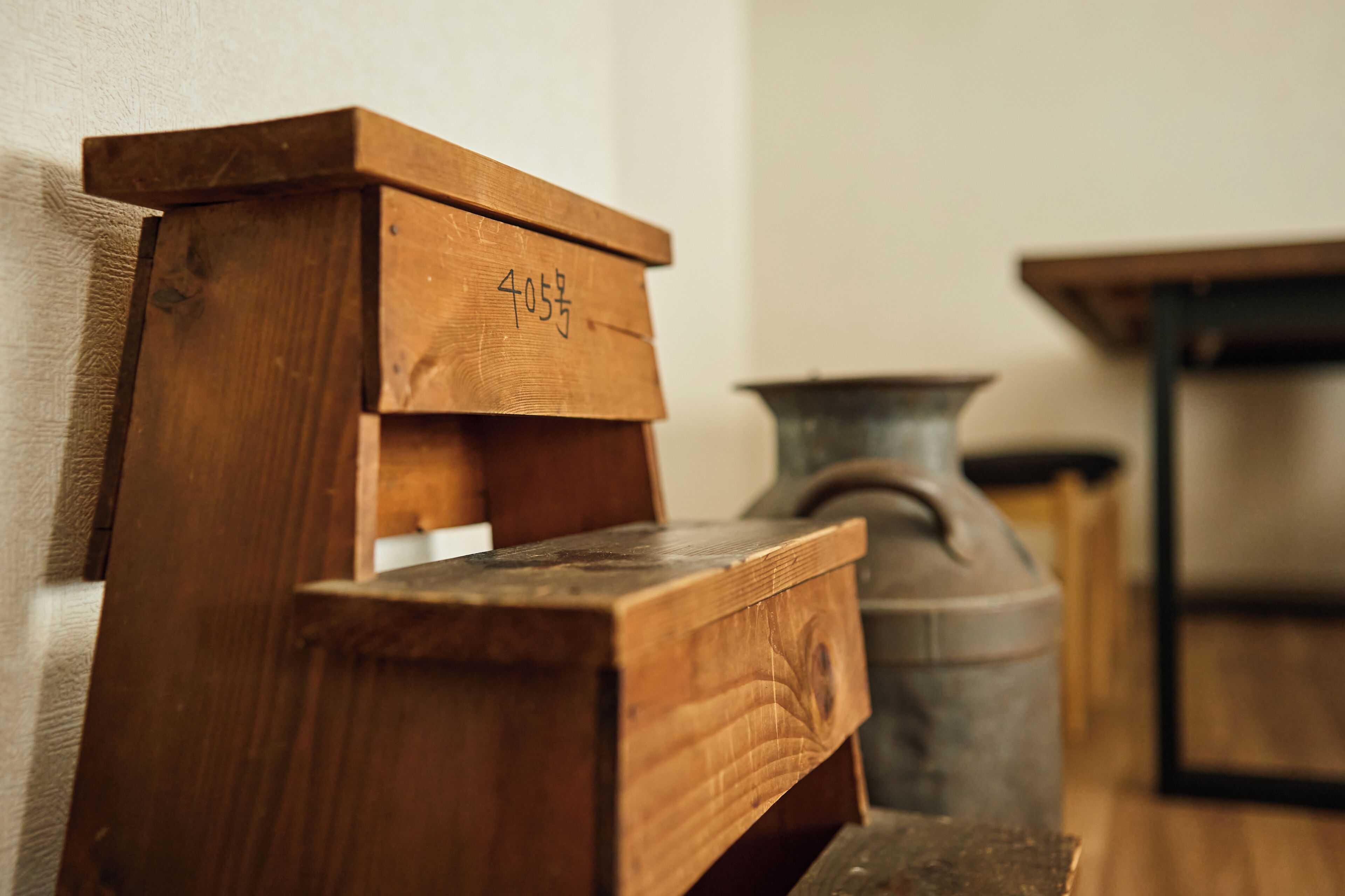 A wooden cabinet with drawers, a metal vase, and a table in a room with wooden flooring.