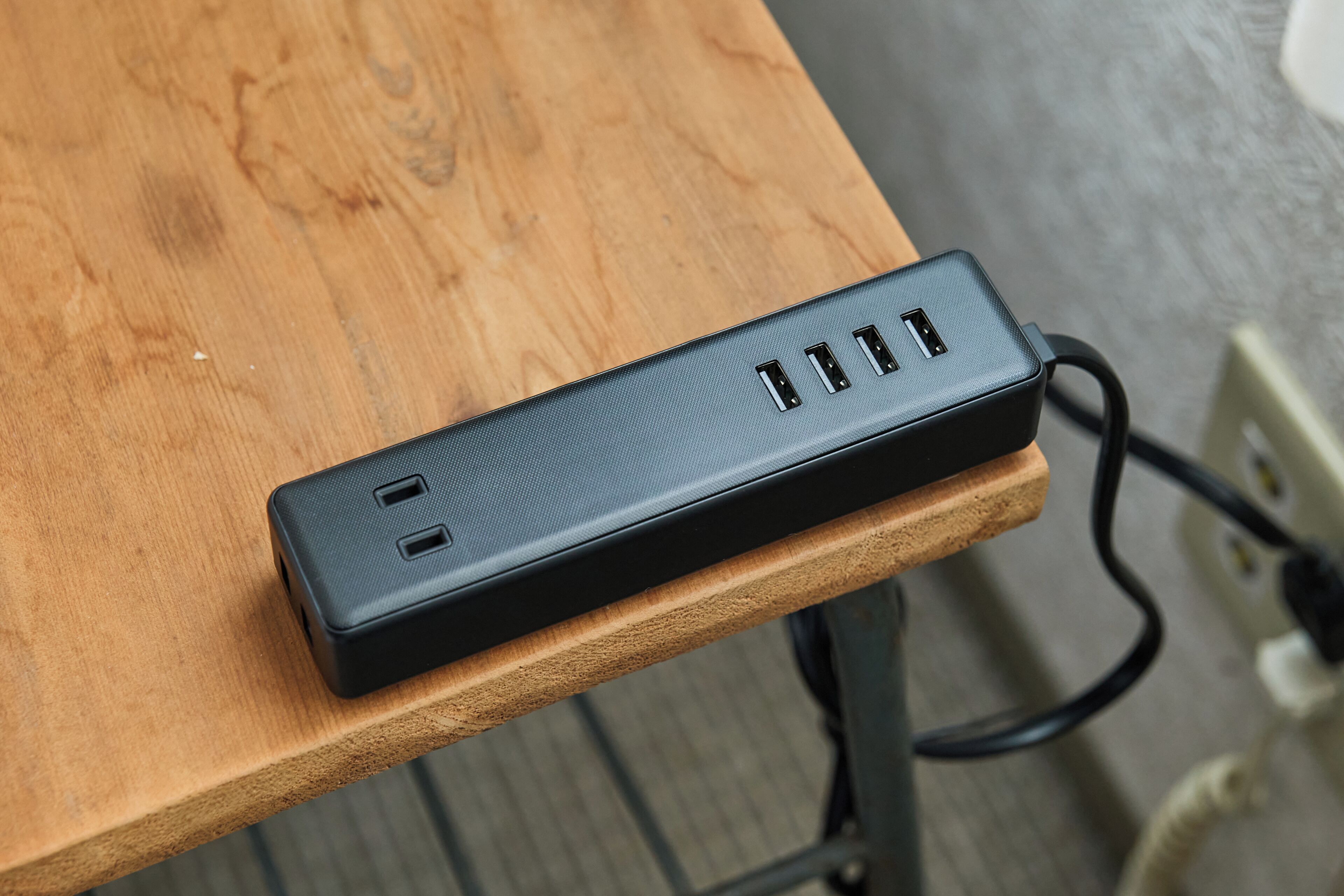 Uma régua de energia preta com várias portas USB sobre uma mesa de madeira.