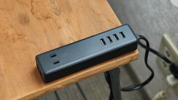 Uma régua de energia preta com várias portas USB sobre uma mesa de madeira.