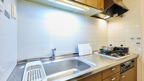 A kitchen with a stainless steel sink, wooden cabinets, a gas stove, and a white tiled backsplash. - Fine court Yamahana (Sapporo)