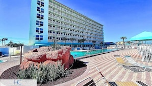 Un hôtel doté d’un espace piscine, d’un grand rocher décoratif et d’une terrasse carrelée avec des chaises longues.