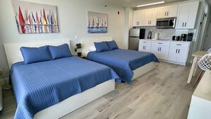 Une chambre d’hôtel avec deux lits, une kitchenette et des œuvres d’art accrochées aux murs.