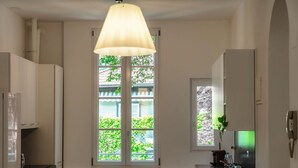 Eine Küche mit Fenster, einer Hängelampe und einer Arbeitsplatte mit Wasserkocher.