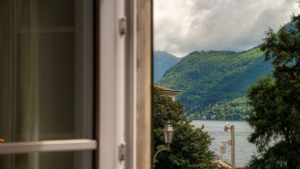 Blick durch ein Fenster auf einen See mit Bergen, Bäumen und einem Laternenpfahl.