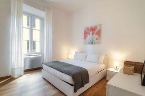 A bedroom with a bed, bedside tables, a radiator, a window with curtains, and a wall-mounted painting. - Sandy - MyHomeinComo (Cernobbio)