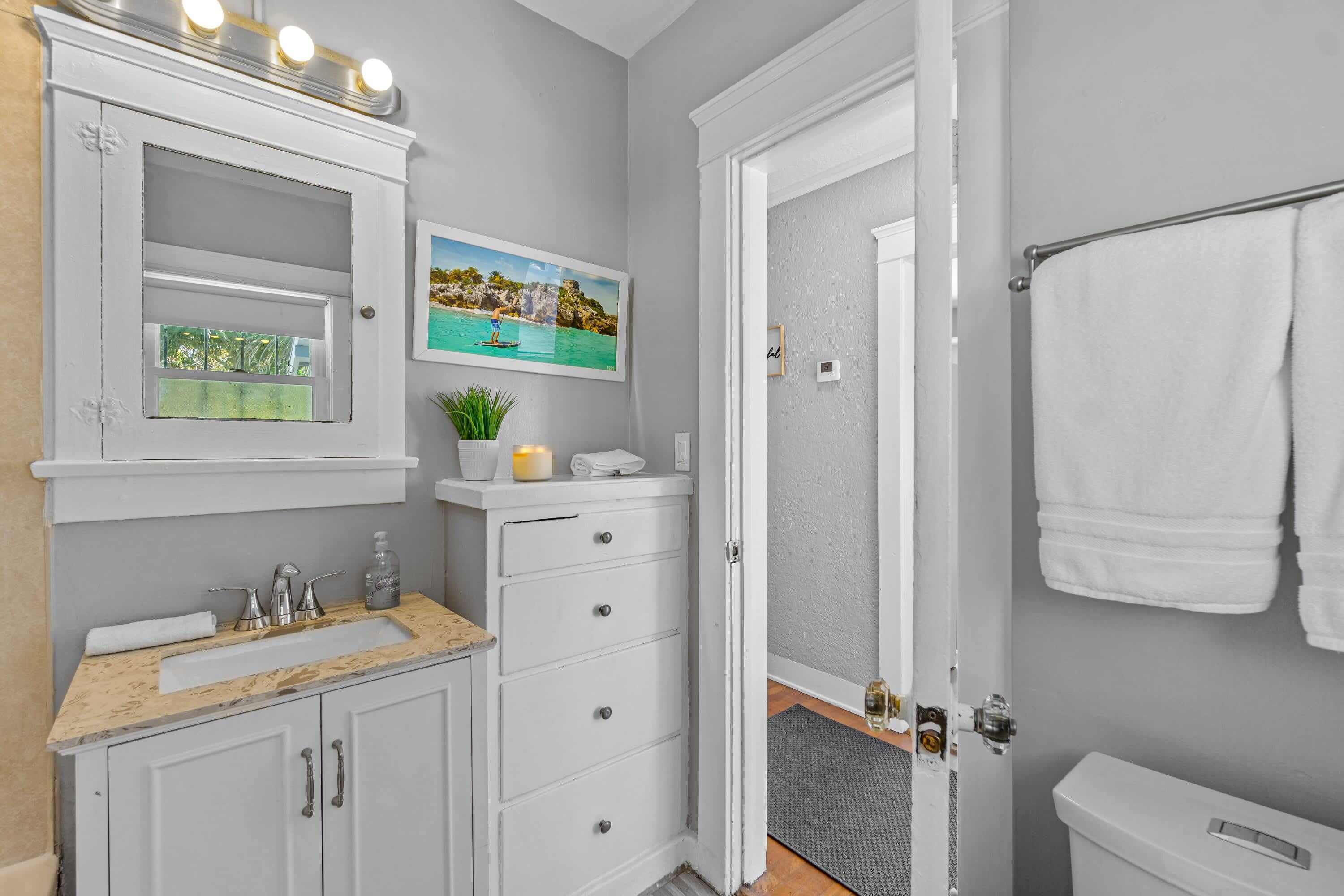 A bathroom with a white vanity, a sink, a mirror, and a towel rack.