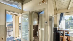 Ein kompaktes Zimmer mit einer Schiebetür, die auf einen Balkon führt, einer kleinen Küchenzeile mit einem Kühlschrank und einem Fenster mit Blick ins Freie.