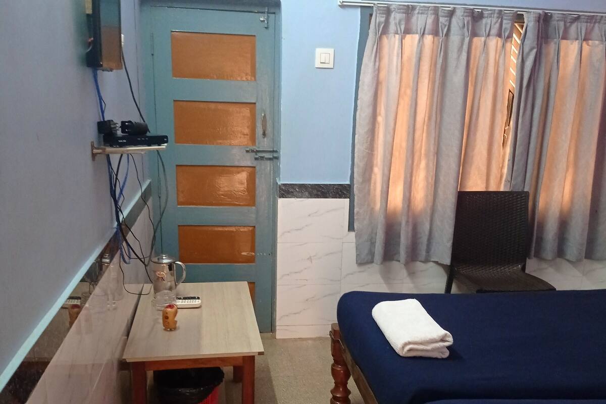 A small, tidy room with a bed, a table, a chair, and a TV mounted on the wall.