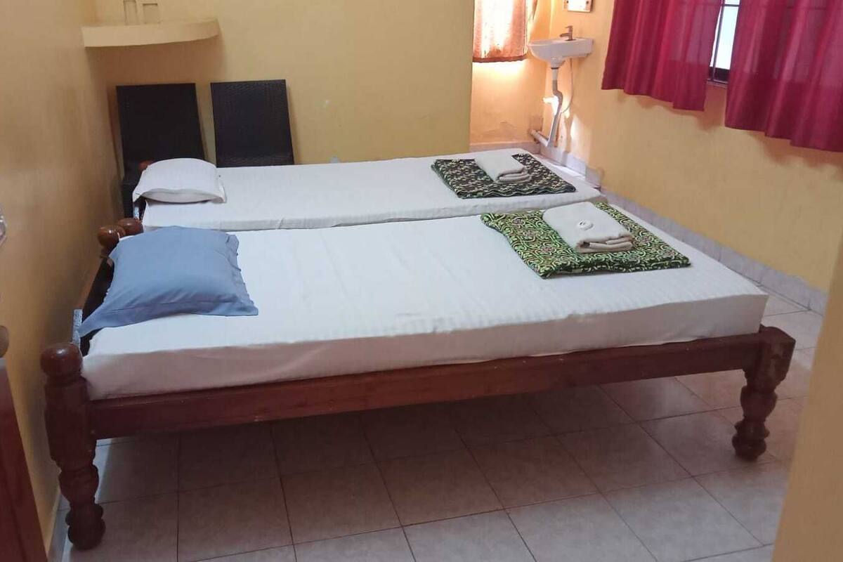 A room with two single beds, a wooden wardrobe, a small shelf, and a bedside table with a lamp.