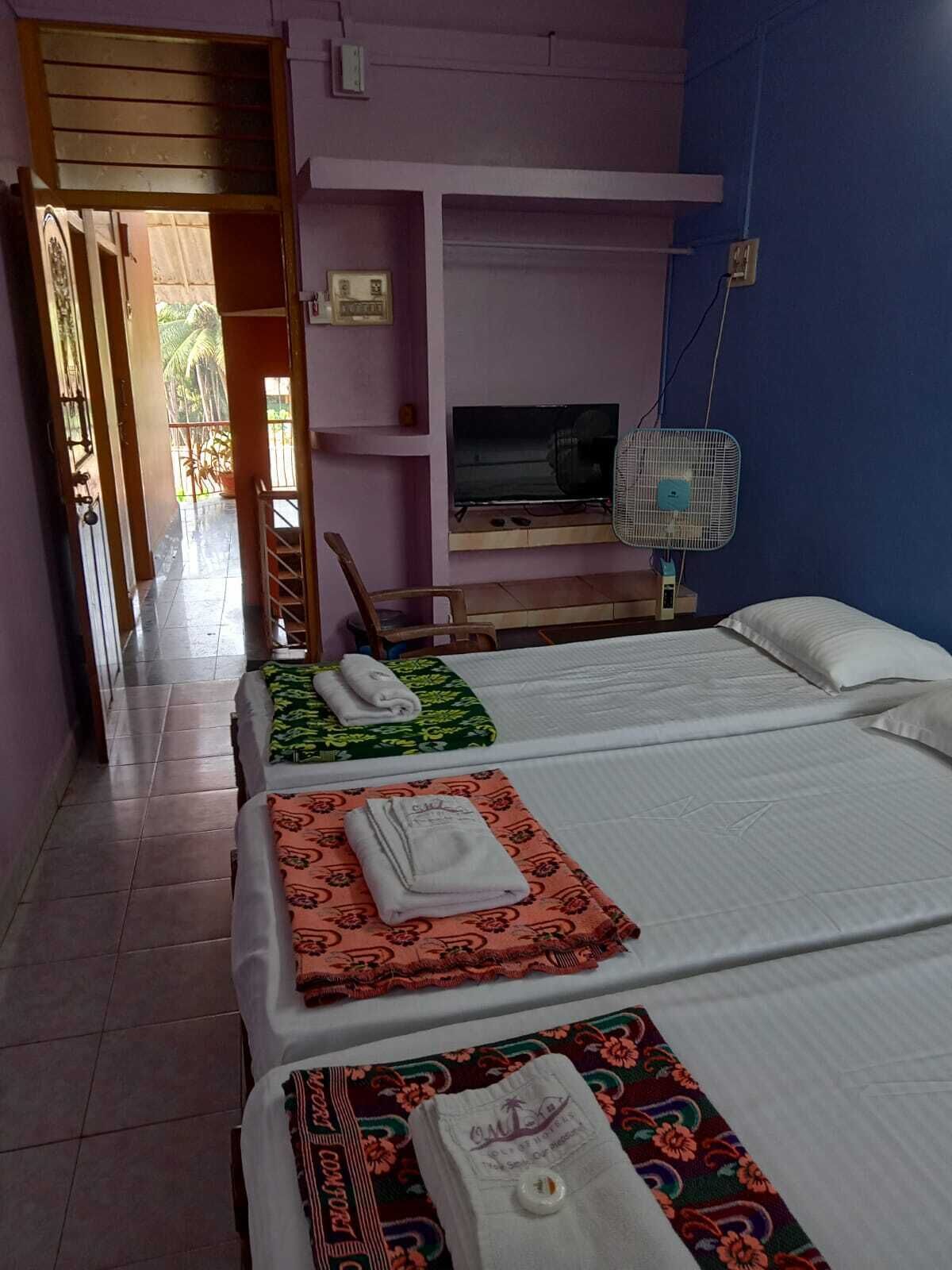 A hotel room with two beds, a TV, a fan, and a view of the outside.