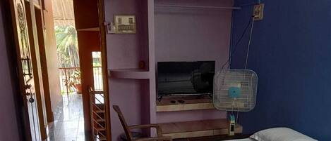 A hotel room with two beds, a TV, a fan, and a view of the outside.