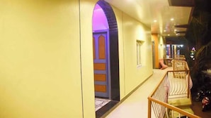 A corridor with a yellow wall, an archway leading to a room, and a seating area with chairs. - Hotel Greens (Kumta)