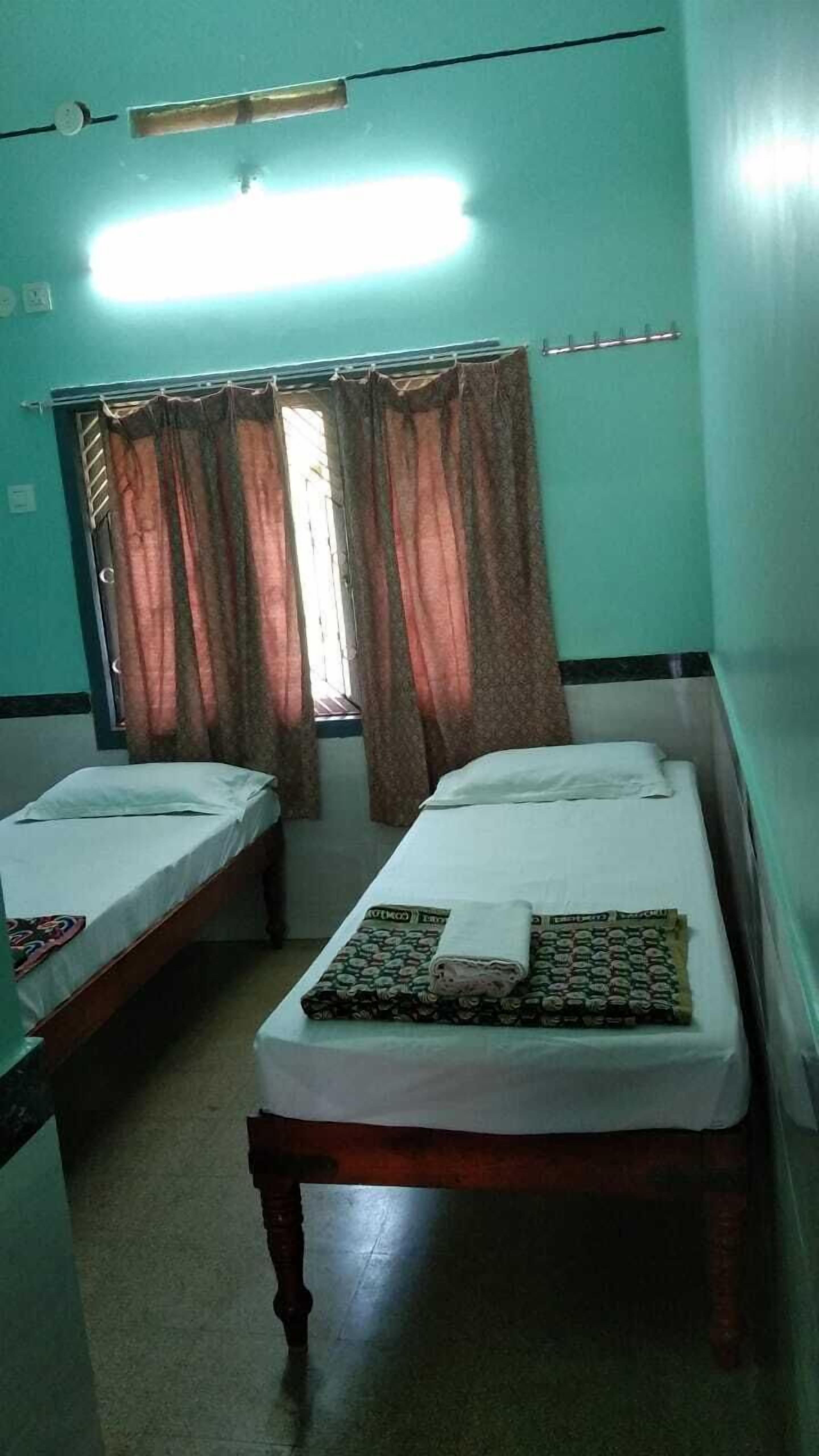 Quarto com duas camas individuais, janela com cortinas e ventoinha no teto.