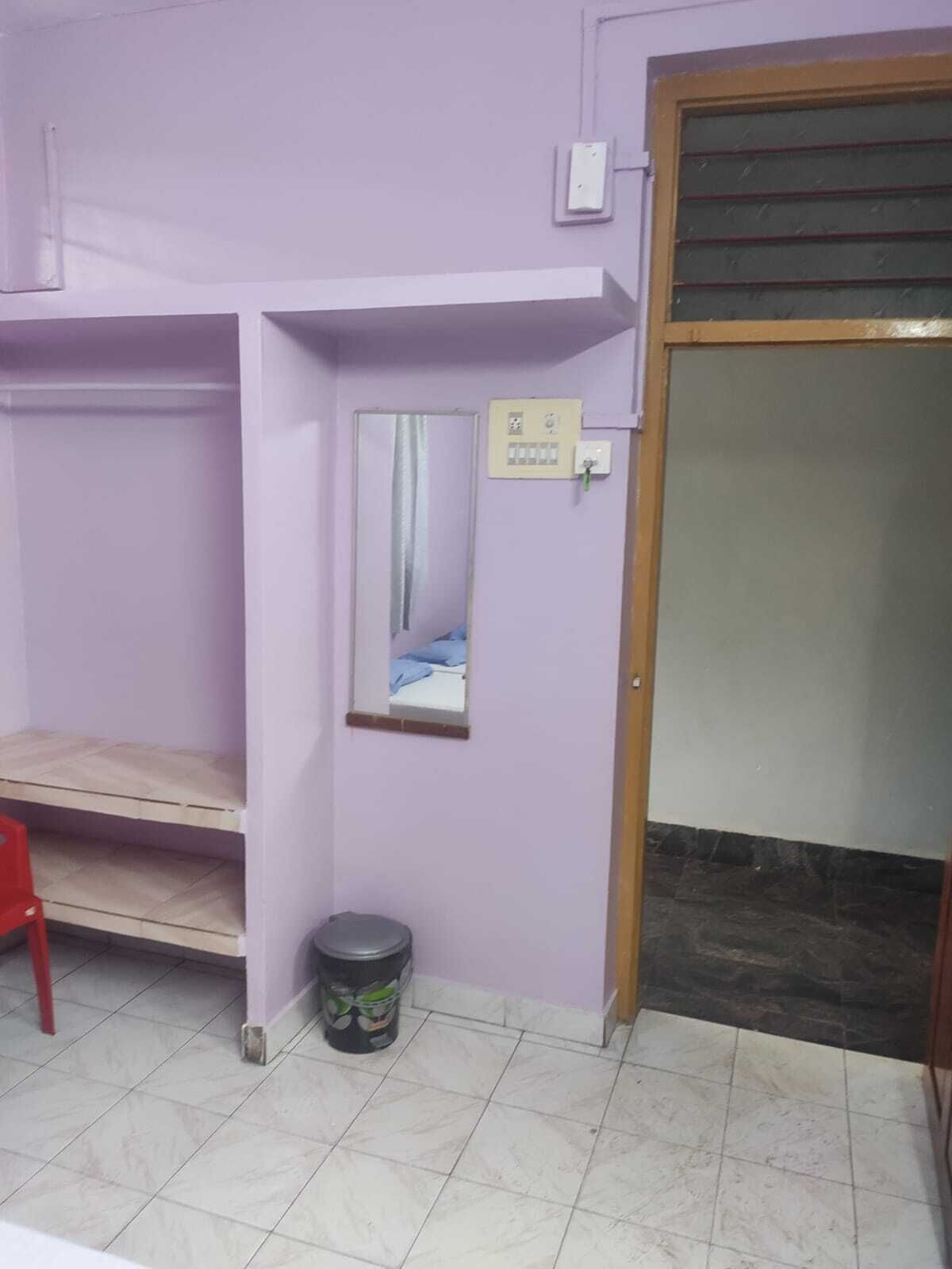 A room with a purple wall, a wooden door, a small trash bin, and a red chair.
