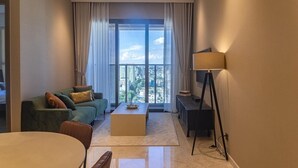 A modern living room with a sofa, coffee table, and a view of a cityscape through large windows. - The MARQ  By An Gia Hospitality (Ho Chi Minh City)