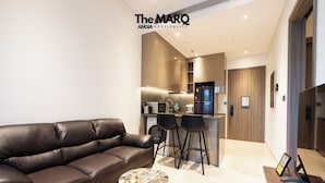 A modern living room with a leather sofa, a small round table, and a kitchen area with a bar. - The MARQ  By An Gia Hospitality (Ho Chi Minh City)